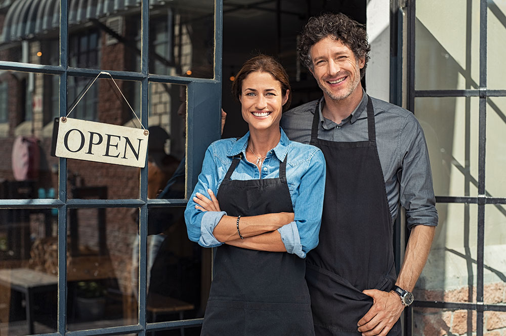 couple standing in front of new store with open sign smiling