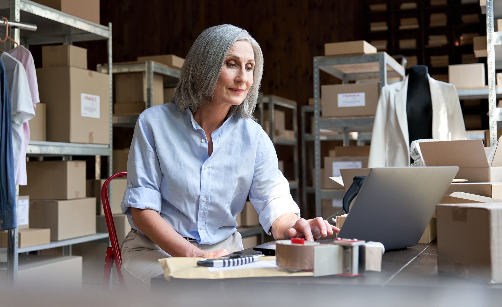 Mature female seller using computer checking ecommerce clothing orders.